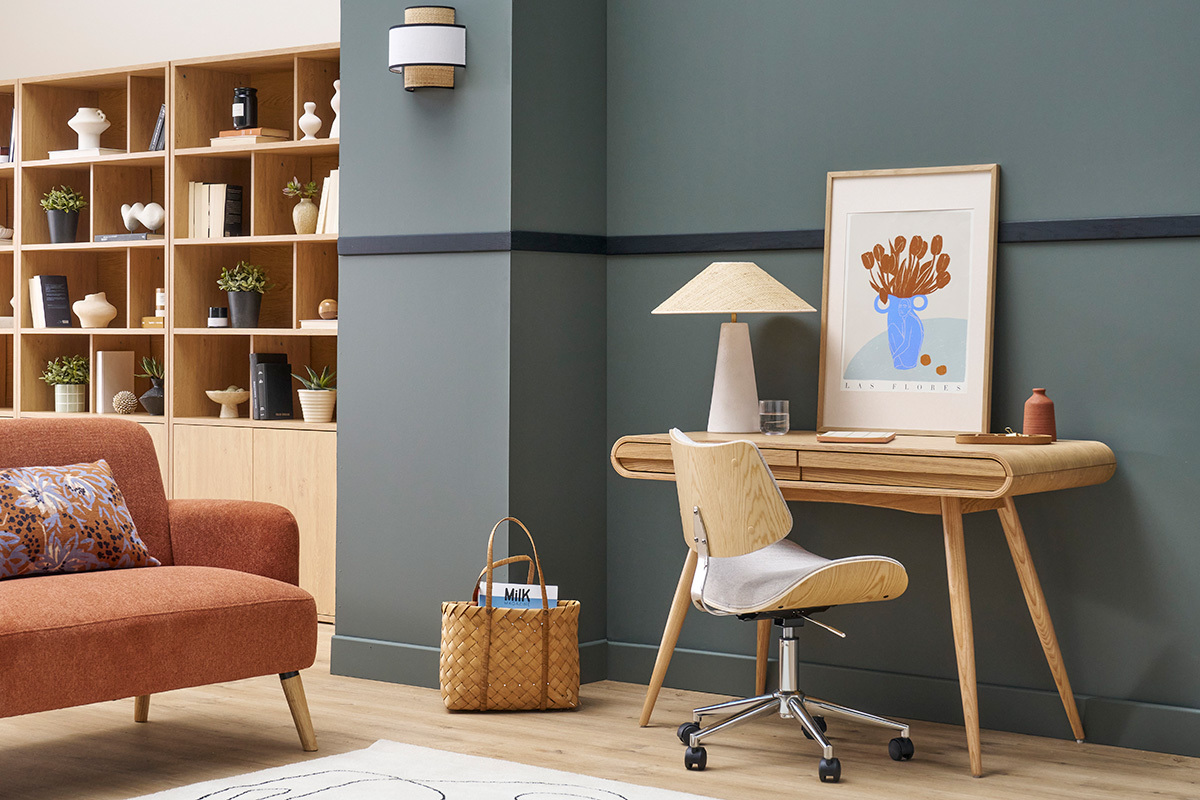 Bureau scandinave bois clair avec lampe et chaise devant un mur gris.