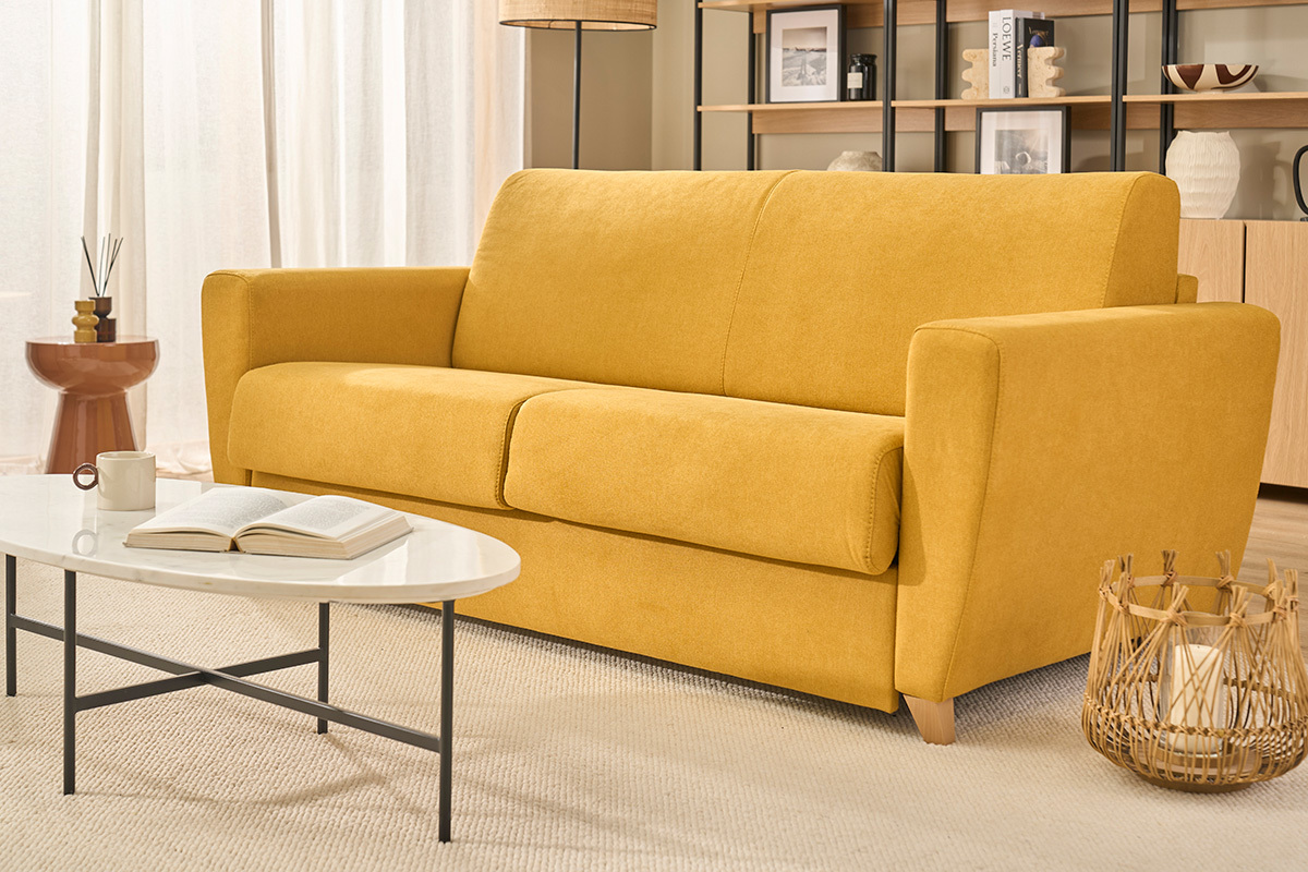 Canap� convertible 3 places jaune moutarde en tissu, vue de face, avec table basse et objets d�co.