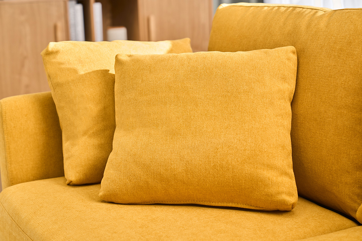 Gros plan sur des coussins d'un canap� en tissu effet velours jaune moutarde.