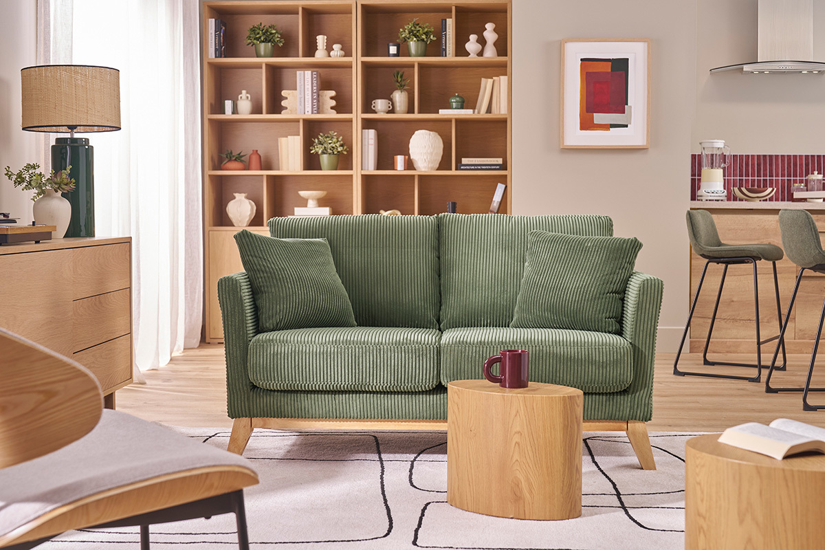 Canap� scandinave vert kaki en velours c�tel� devant une �tag�re en bois clair, vue de face.
