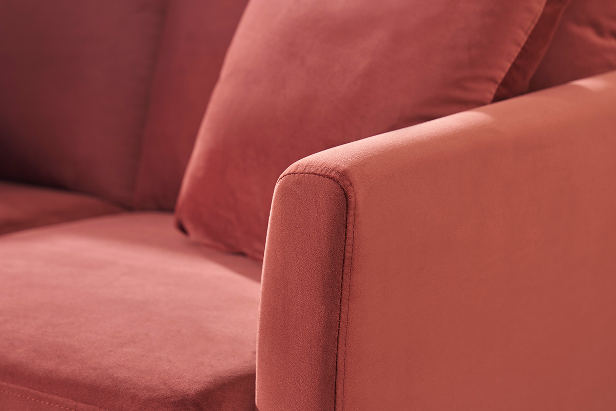 Gros plan sur un canap� scandinave en velours rouge tomette avec un accoudoir et coussin visible.