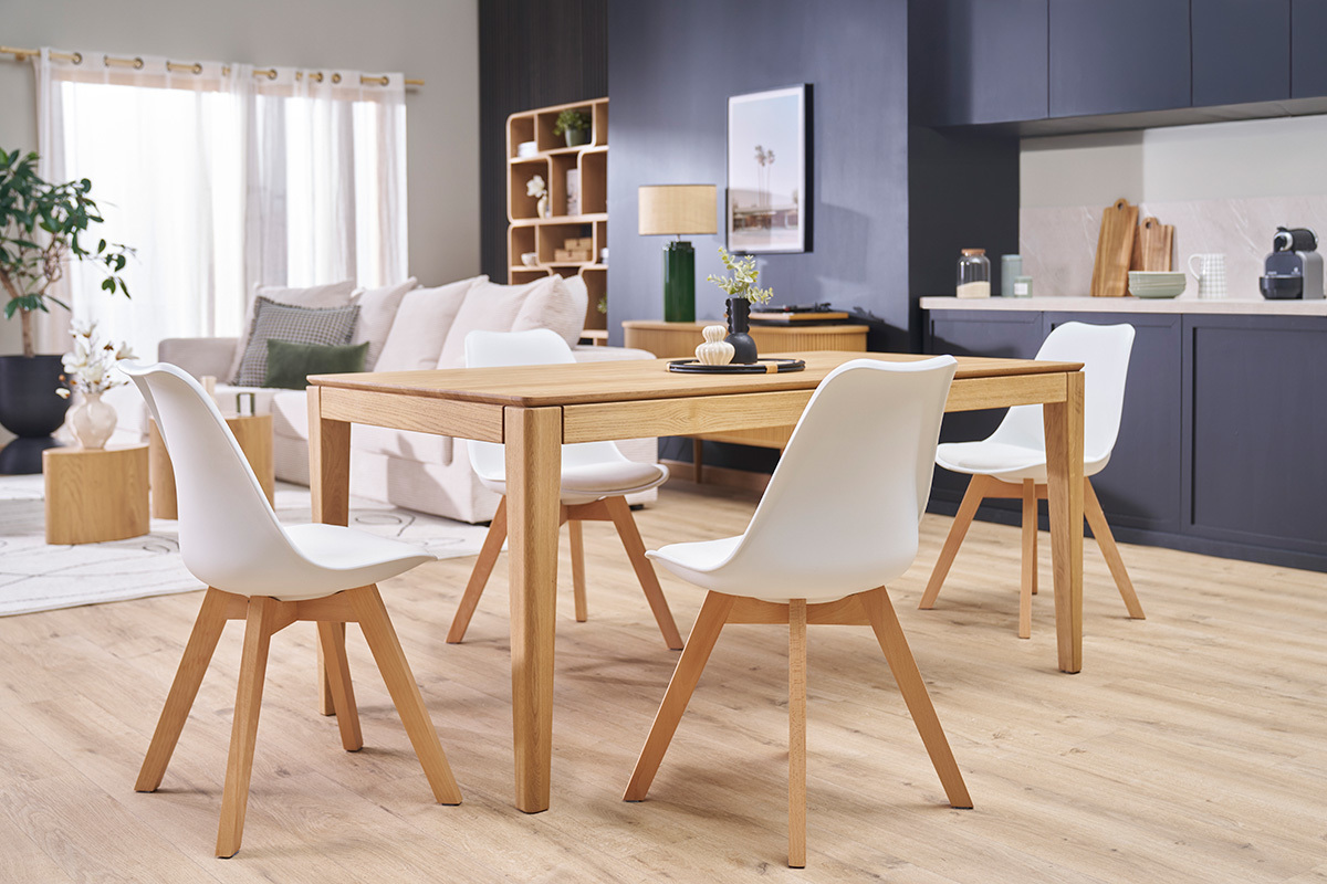 Lot de 4 chaises scandinaves blanches avec pieds en bois clair autour d'une table en bois.