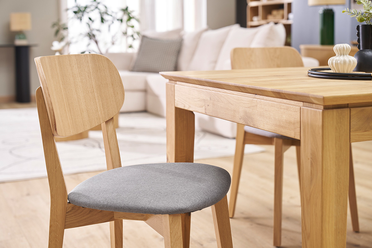 Chaise vintage en bois clair avec assise en tissu gris clair devant une table en bois.
