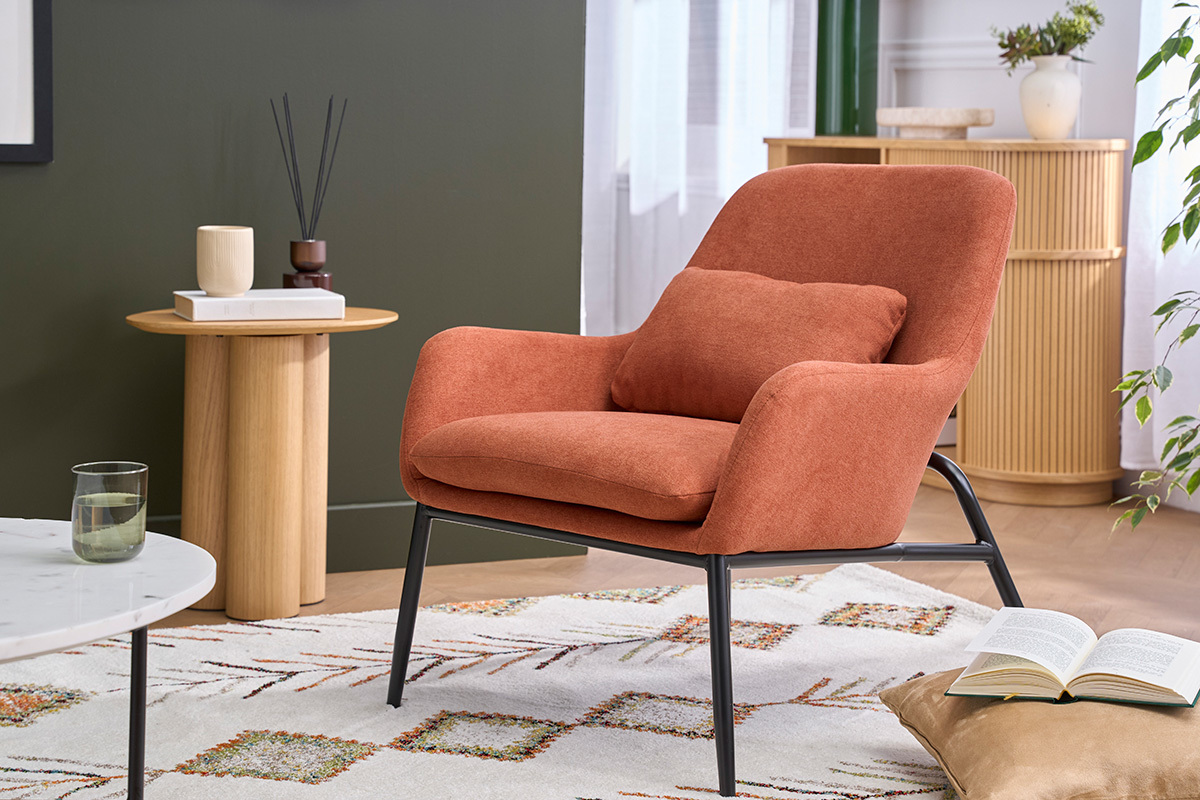 Fauteuil en tissu effet velours terre brul�e avec pieds en m�tal, angle 3/4, � c�t� d'une table en bois.