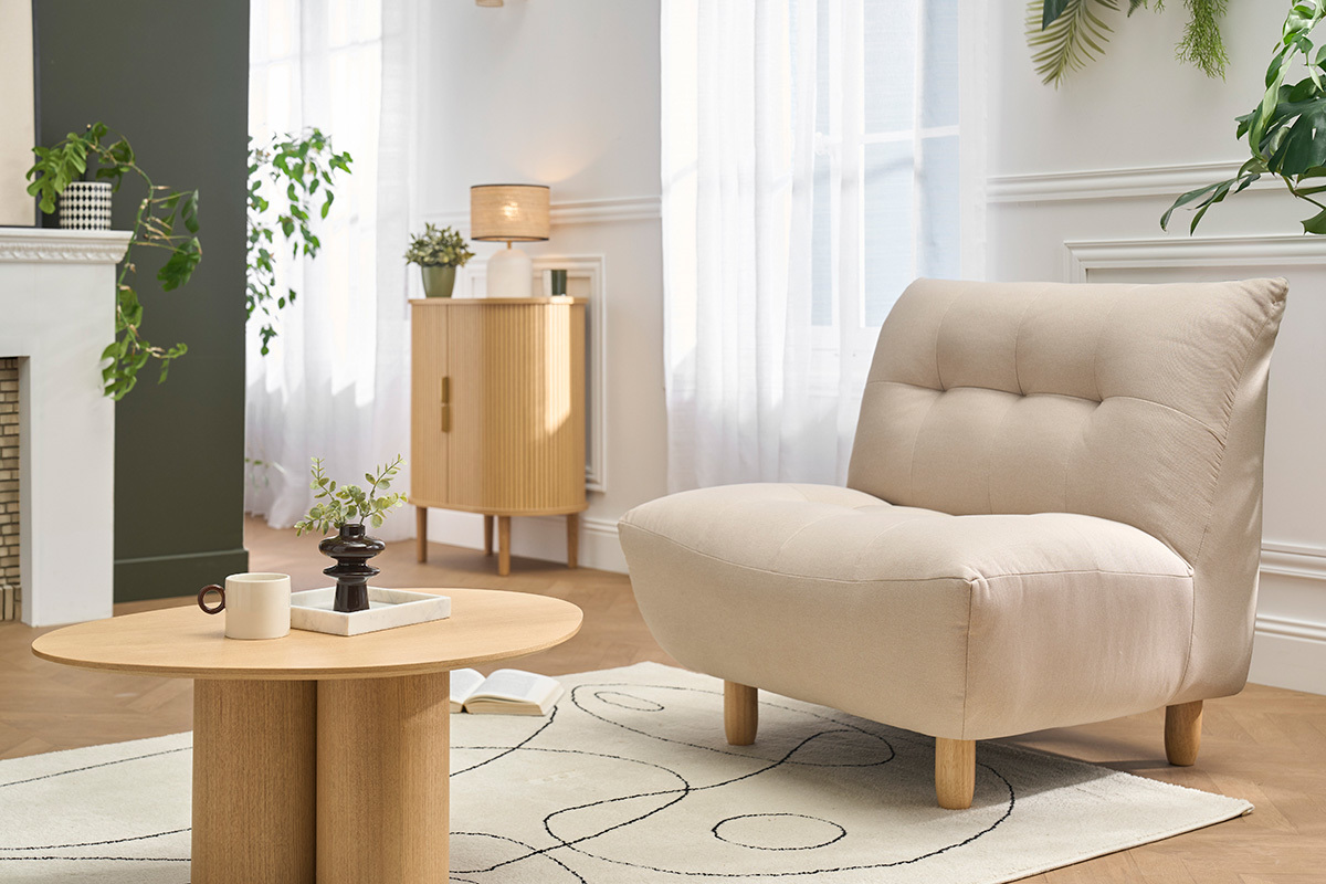 Fauteuil scandinave beige YUMI avec coussins dans un salon moderne, vue de 3/4.