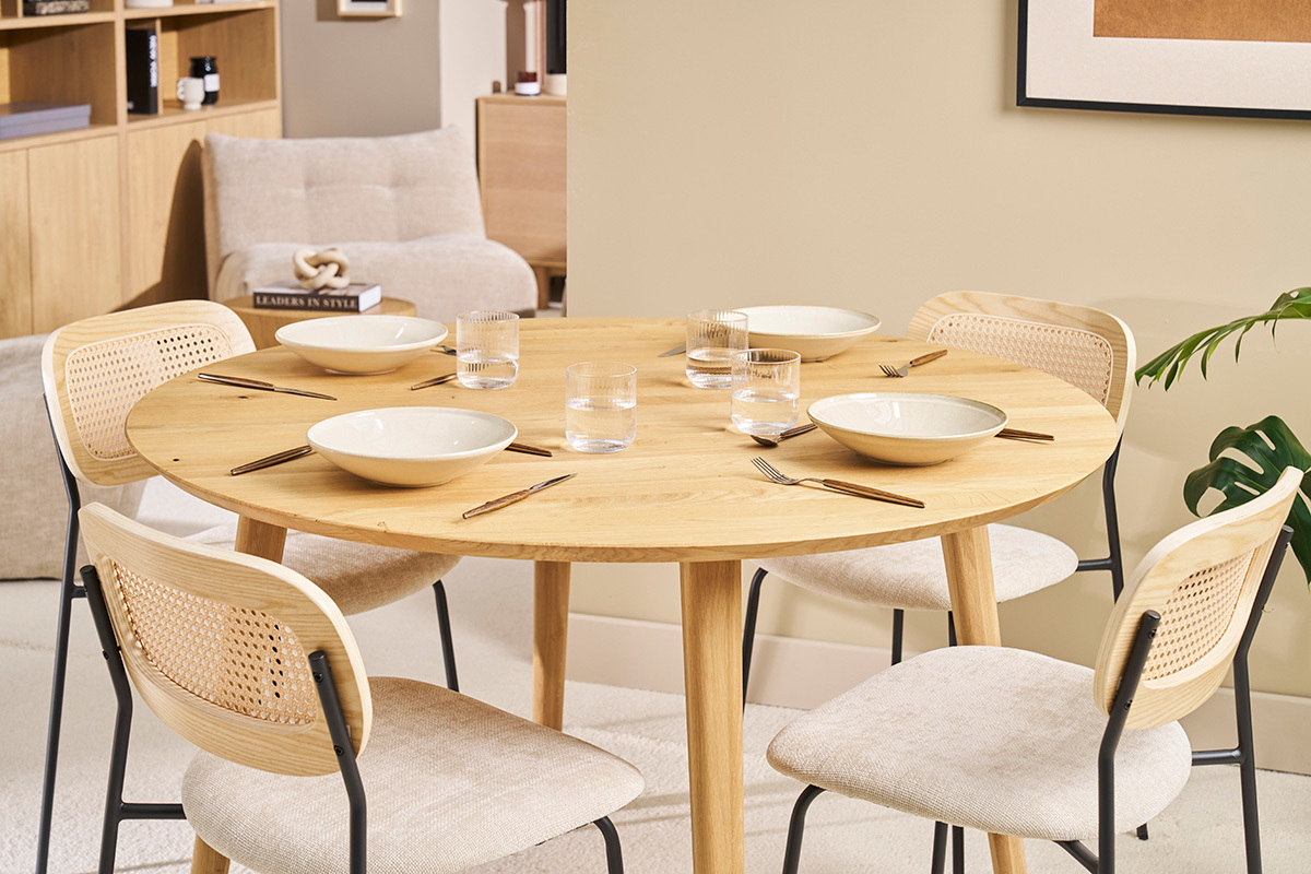 Table ronde en ch�ne clair avec couverts et assiettes, entour�e de chaises dans une salle � manger.